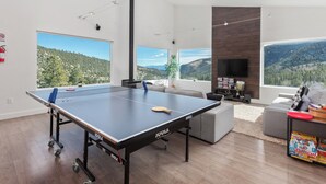 Uma sala de estar espaçosa com mesa de pingue-pongue, lareira e grandes janelas com vista para as montanhas.