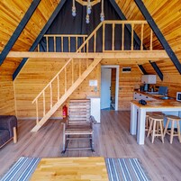 Un interior de madera con un dormitorio en entrepiso, una zona de cocina y una escalera.