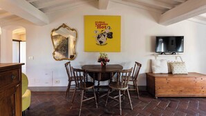 Een eetgedeelte met een houten tafel, stoelen, een spiegel, een televisie en een poster aan de muur.