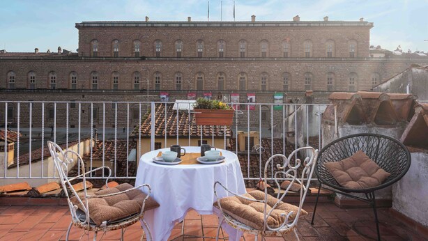 Een terras met een tafel gedekt voor twee, twee rieten stoelen, een hangplant en een bakstenen gebouw op de achtergrond.