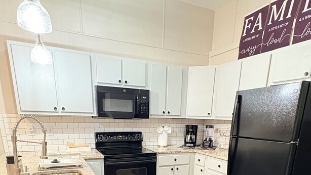 Een moderne keuken met witte kasten, een zwarte koelkast, een magnetron en een fornuis.