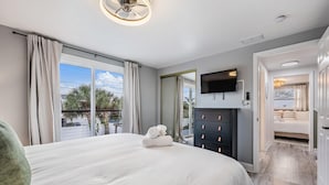Un dormitorio con una cama grande, un televisor montado en la pared y vistas al exterior a través de la ventana.