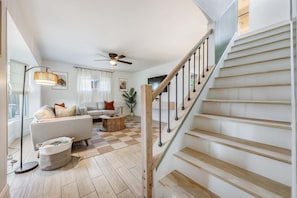 Ein geräumiges Wohnzimmer mit Treppe, Deckenventilator und großem Fenster mit Vorhängen.