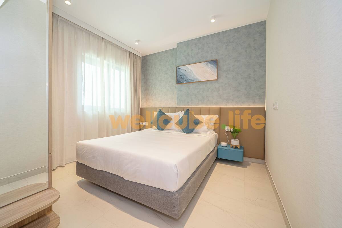 A modern hotel room with a large bed, a bedside table with a lamp, and a painting on the wall.