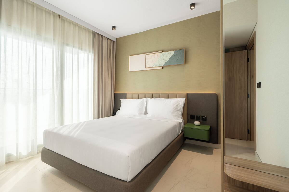 A modern hotel room with a large bed, a nightstand, a mirror, and a painting on the wall.