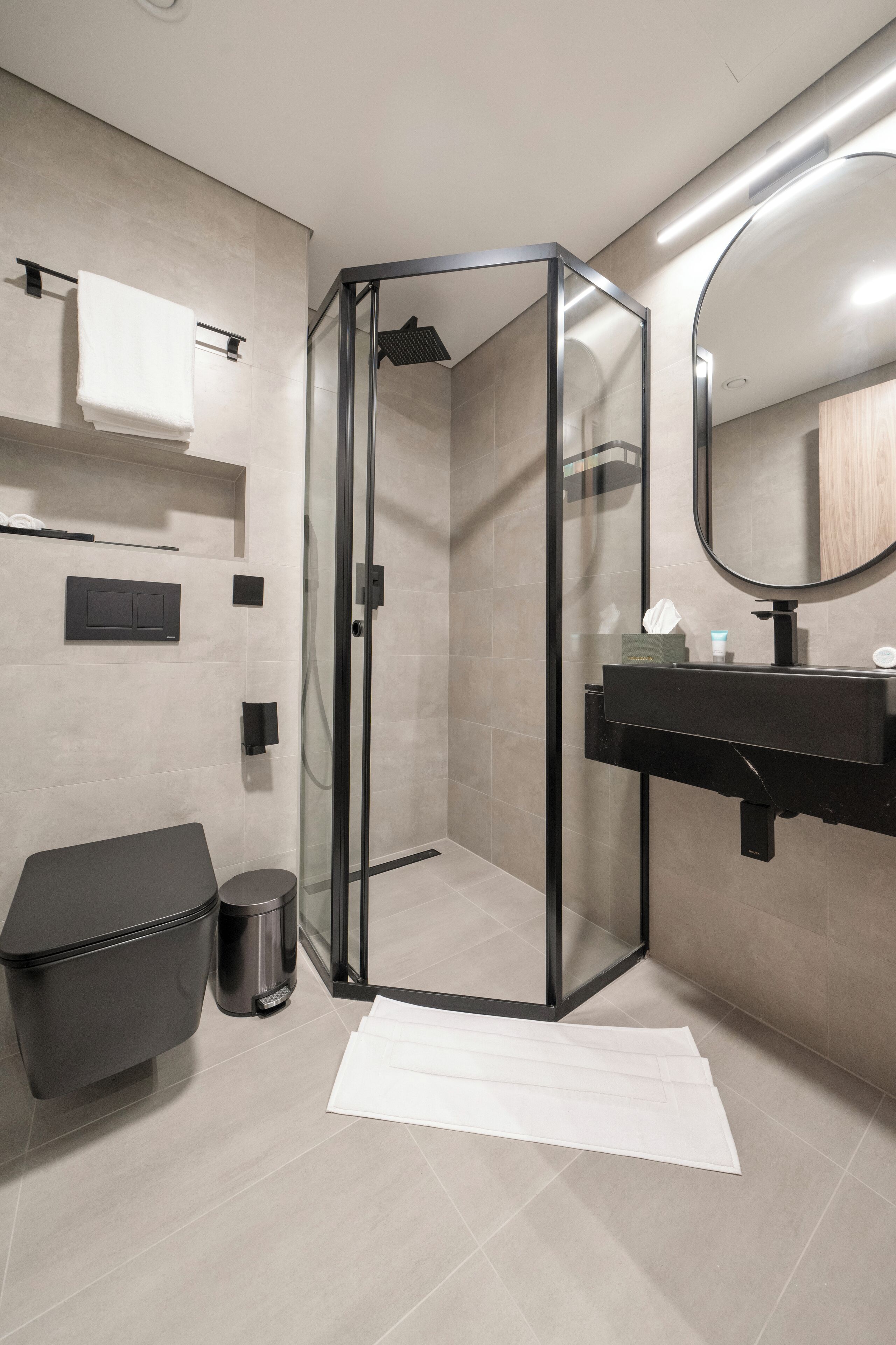 Ein modernes Badezimmer mit einer in Glas eingefassten Dusche, einem schwarzen Waschbecken und einem weißen Handtuch auf dem Boden.