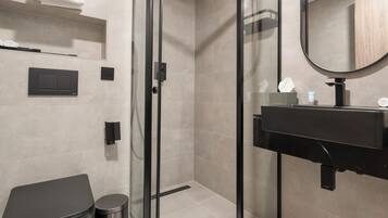 Ein modernes Badezimmer mit einer in Glas eingefassten Dusche, einem schwarzen Waschbecken und einem weißen Handtuch auf dem Boden.