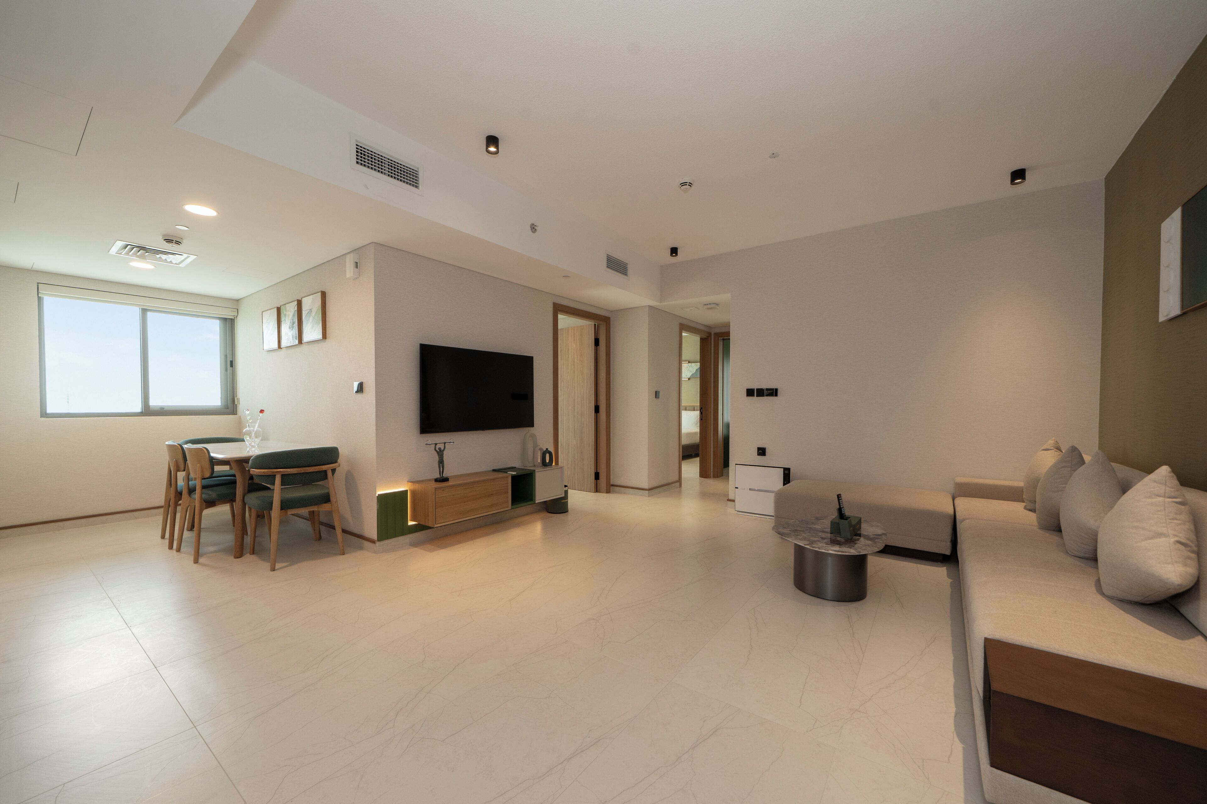 A spacious living area with a flat-screen TV, a sofa, a dining table with chairs, and a coffee table.