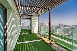 Un balcón con vistas a un paisaje urbano, un área con césped y una silla lounge de madera.