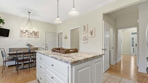 A kitchen with a marble countertop, white cabinets, a dining area with a table and chairs, and pendant lighting. - Forget-Me-Not: Spacious 6-Bedroom Retreat, Walk to Downtown (Highlands)