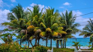A white car parked in a driveway with a view of the ocean and palm trees. - 3-bedroom ocean front bungalow in delightful Long Bay, Portland w AC ,Ocean View (Long Bay)