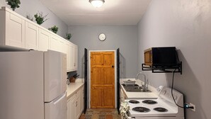 A compact kitchen with white cabinets, a wooden door, a microwave shelf, a stove, and a clock on the wall. - 3-bedroom ocean front bungalow in delightful Long Bay, Portland w AC ,Ocean View (Long Bay)