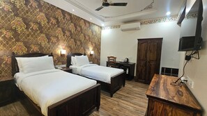 A hotel room with two beds, a wooden wardrobe, a desk, and a television. - Hotel Ranavilas Palace (Jaipur)