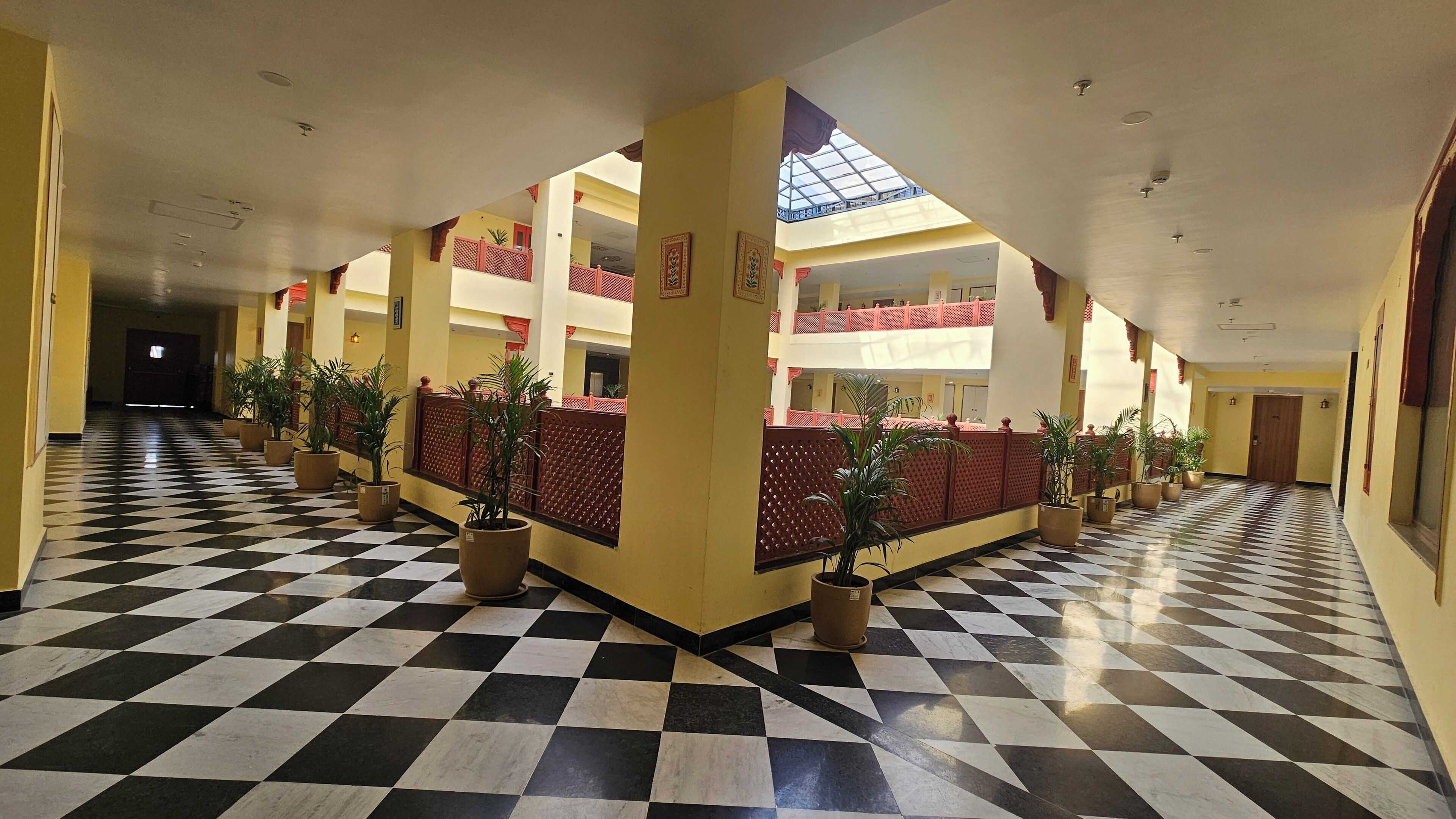 Eine Hotellobby mit Schachbrettfußboden, Topfpflanzen und einem offenen Innenbereich, der von einem roten Gitterzaun begrenzt wird.