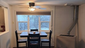 Ein Essbereich mit Tisch und Stühlen, ein Fenster mit Blick auf Bäume und ein Wandlüfter.