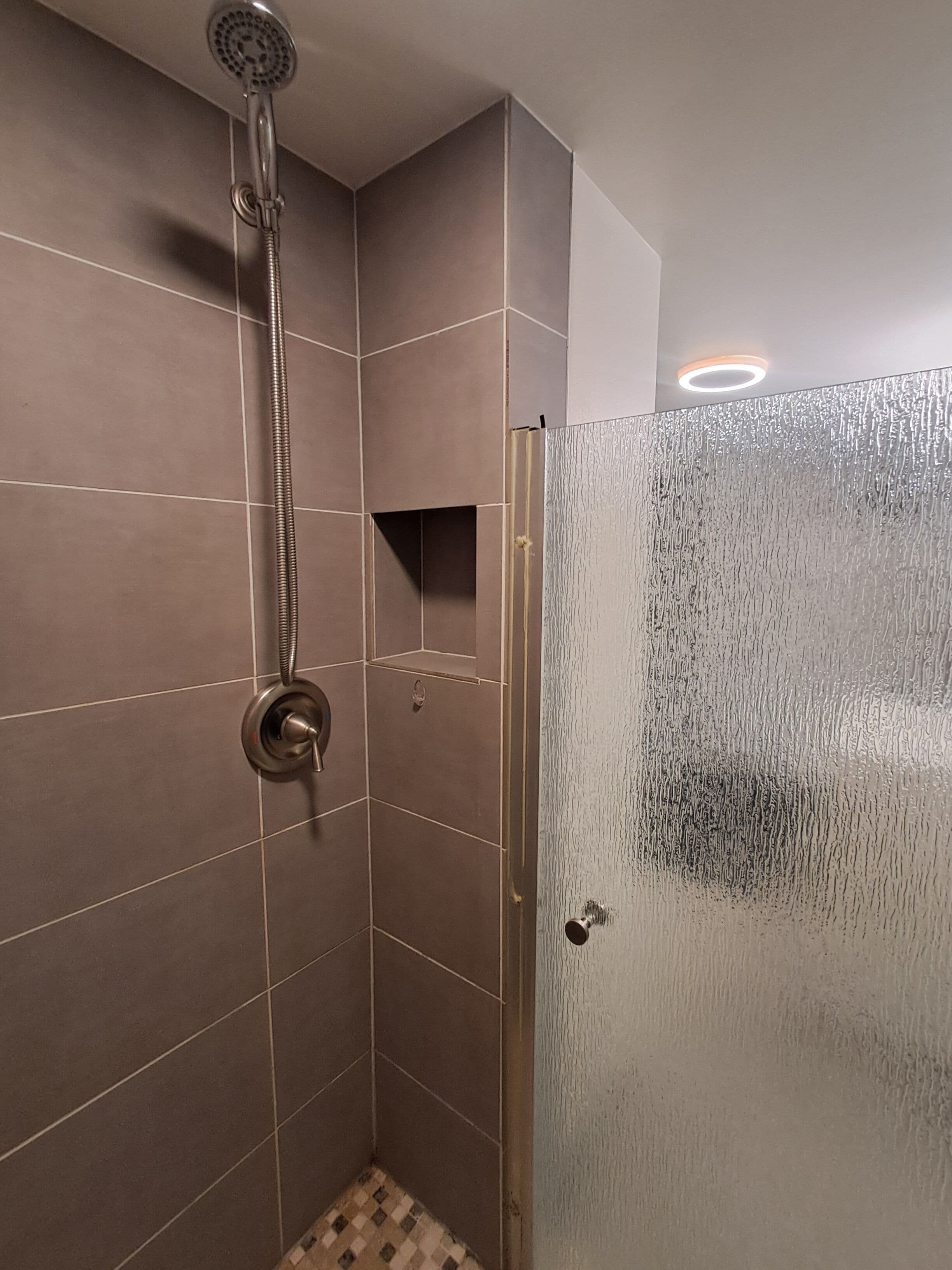 A shower area with a glass door, tiled walls, and a showerhead.