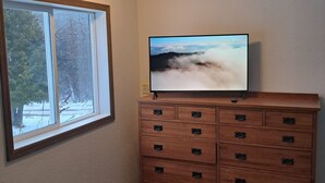Ein Zimmer mit großem Fenster, einem Holzkoffer und einem wandmontierten Flachbildfernseher.