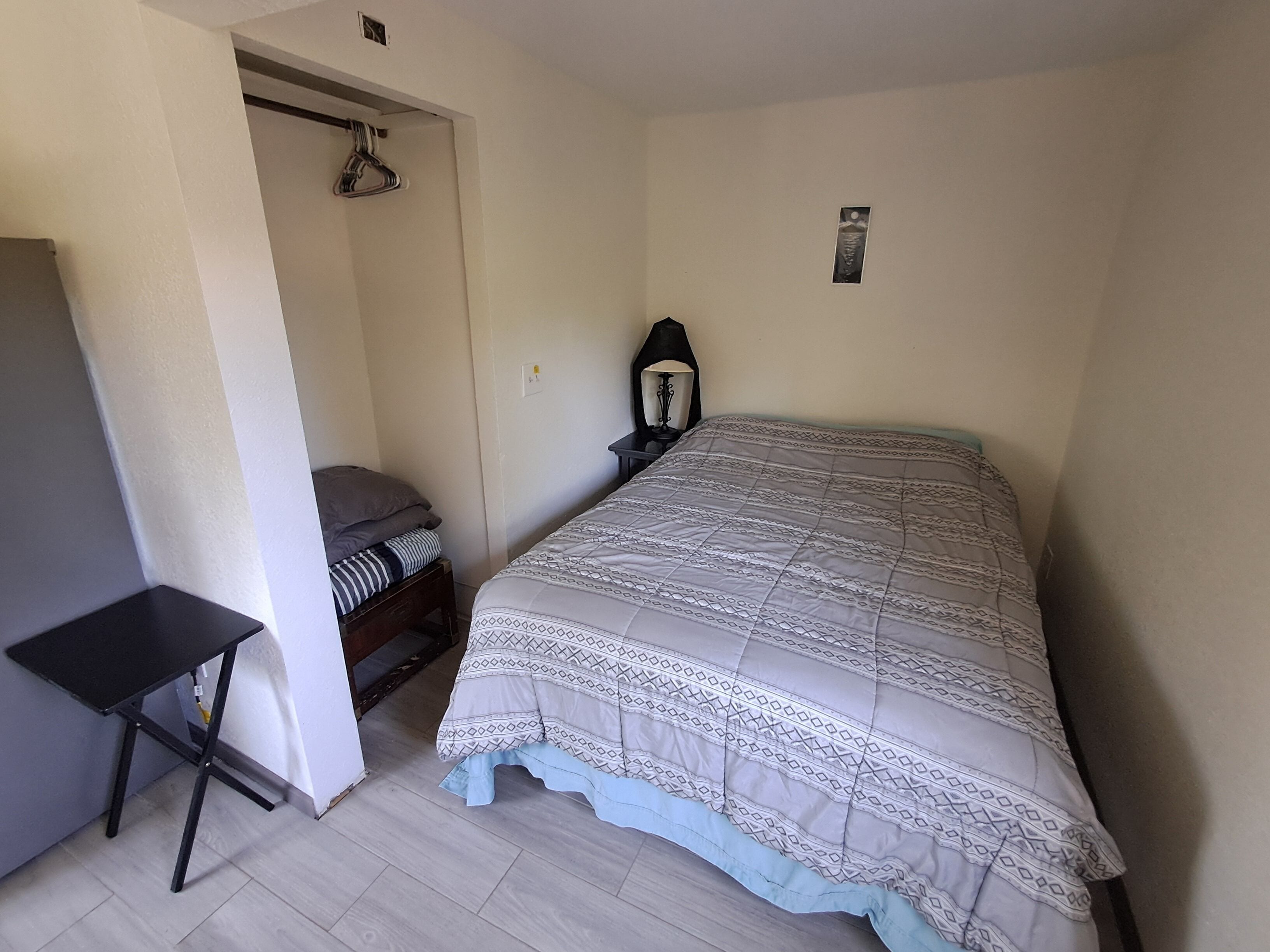 Une chambre à coucher avec un lit, une table de chevet, une lampe, une armoire et une petite table.