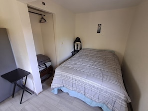 A bedroom with a bed, a nightstand, a lamp, a wardrobe, and a small table.