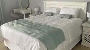 Una cama bien hecha con cabecera blanca, una mesita de noche con lámpara y un aire acondicionado instalado en la pared.