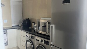 Una cocina compacta con un refrigerador de acero inoxidable, un microondas, una cafetera y una lavadora.