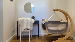 Een babyschommel met een grijze stoffen zitting, een witte pluizige fauteuil, en een ronde spiegel aan de muur.