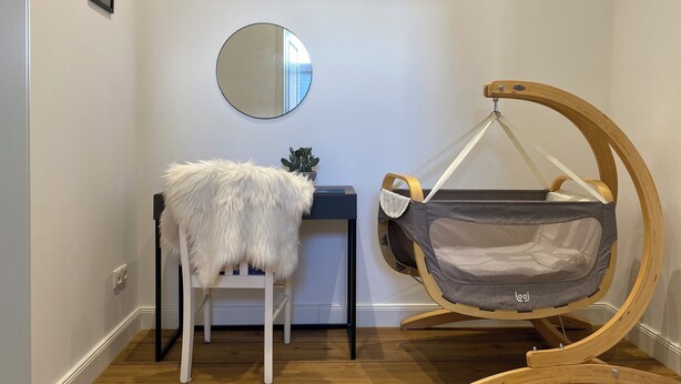 A baby rocker with a grey fabric seat, a white furry chair, and a round mirror on the wall. - 'sea dreams' | Chic design apartment #Octopus Seapearl - Central at main station (Schwerin)