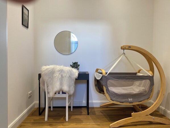 Una mecedora para bebés con asiento de tela gris, un sillón blanco de pelo y un espejo redondo en la pared.