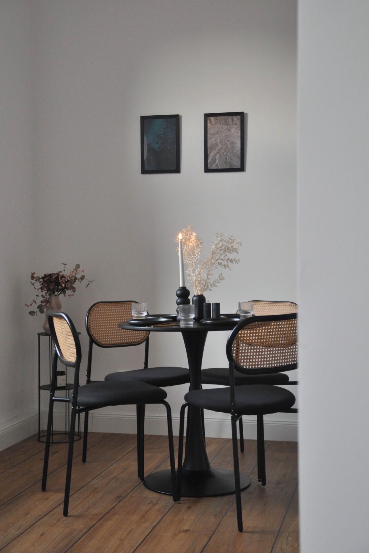 A dining area with a round table, four chairs, a candle, and two framed pictures on the wall.