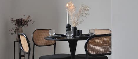 A dining area with a round table, four chairs, a candle, and two framed pictures on the wall.