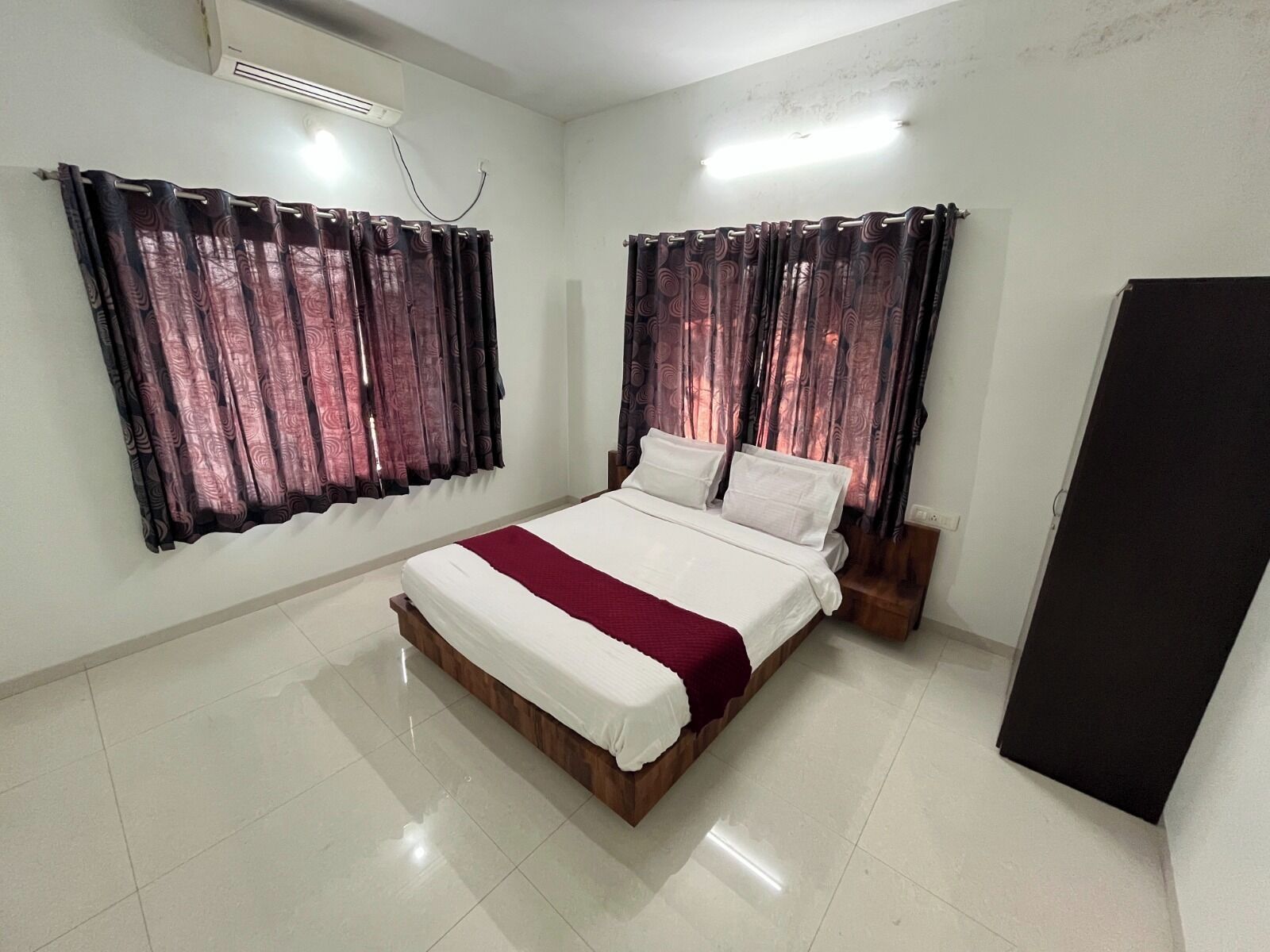 Une chambre à coucher avec un lit, des rideaux, une armoire et un sol carrelé.