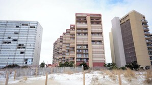 Una propiedad frente a la playa con una playa arenosa, una valla de madera y tres edificios altos al fondo.
