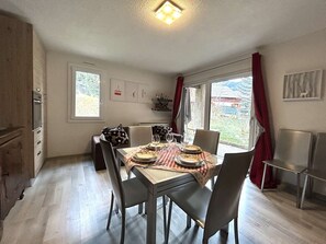 A dining area with a table set for four, chairs, a window with curtains, and a view of the outdoors. - 3-room apartment with garden and parking, Briançon (Briançon)