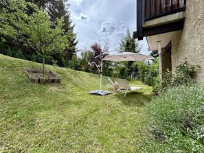 Une cour arrière verdoyante avec un espace patio comprenant une table et des chaises, ainsi qu’une pergola dotée d’un parasol.