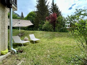 A grassy backyard with two white lounge chairs and a large umbrella.