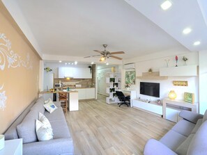A modern living room with a sofa, a TV, and a kitchen in the background. - Elegant Apartment in Torremolinos, 1 Bedroom (Torremolinos)