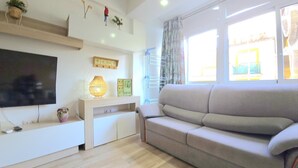 Ein Wohnzimmer mit Flachbildfernseher, einer Couch, einem Couchtisch und einem Fenster mit Vorhängen.
