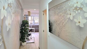 Ein Flur mit einer weißen Wand und einem großen Blumenbild. Im Hintergrund steht ein Blumentopf und eine weiße Bank.