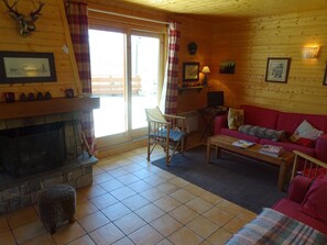 A cozy cabin interior with a fireplace, a red couch, a wooden table, and a television. - Charming 5-Bedroom Chalet, 10 ppl, Vallandry (Peisey-Vallandry)