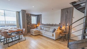 A modern living room with a wooden floor, a sectional sofa, a dining table set for six, and a spiral staircase. - Cozy apt for 6 in Val Thorens, near slopes (Val Thorens)