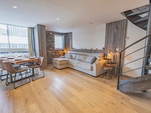 Ein modernes Wohnzimmer mit Holzboden, einer Eckcouch, einem Esstisch für sechs Personen und einer Wendeltreppe.