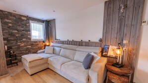A modern living room with a sectional sofa, a wooden accent wall, and a small wooden table with a lamp. - Cozy apt for 6 in Val Thorens, near slopes (Val Thorens)