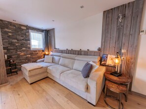 Ein modernes Wohnzimmer mit einer Eckcouch, einer Wandpaneele aus Holz und einem kleinen Holztisch mit einer Lampe.