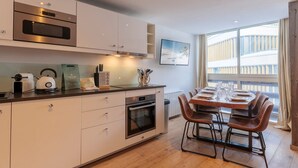 A modern kitchen with white cabinets, stainless steel appliances, and a dining area with wooden table and chairs. - Cozy apt for 6 in Val Thorens, near slopes (Val Thorens)