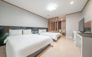 A hotel room with two beds, a desk, a TV, and a window.