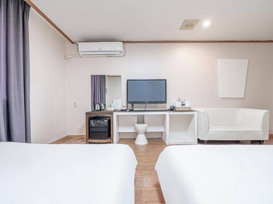 A hotel room with two beds, a desk with a computer, a television, and a small seating area.