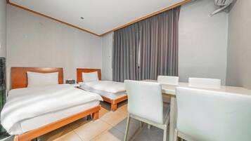 A hotel room with two single beds, a small desk with a chair, and a large window with curtains.