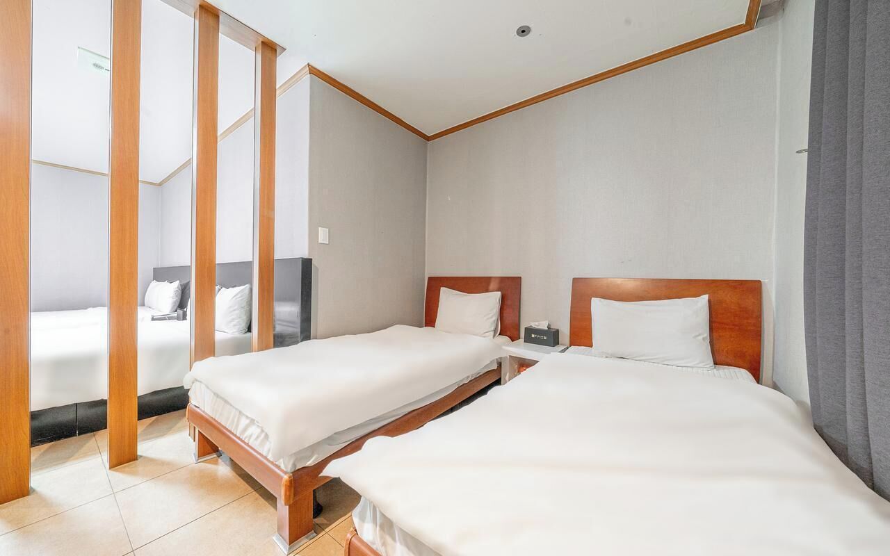Habitación de hotel con dos camas individuales, cabeceros de madera y un ventanal grande.