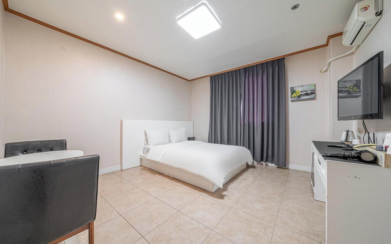 A hotel room with a bed, a desk, a chair, a television, and an air conditioning unit.
