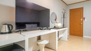 A hotel room with a large flat-screen TV mounted on the wall, a white desk with a kettle, a small stool, and a coat rack. - Hotel Lisa (Donghae)